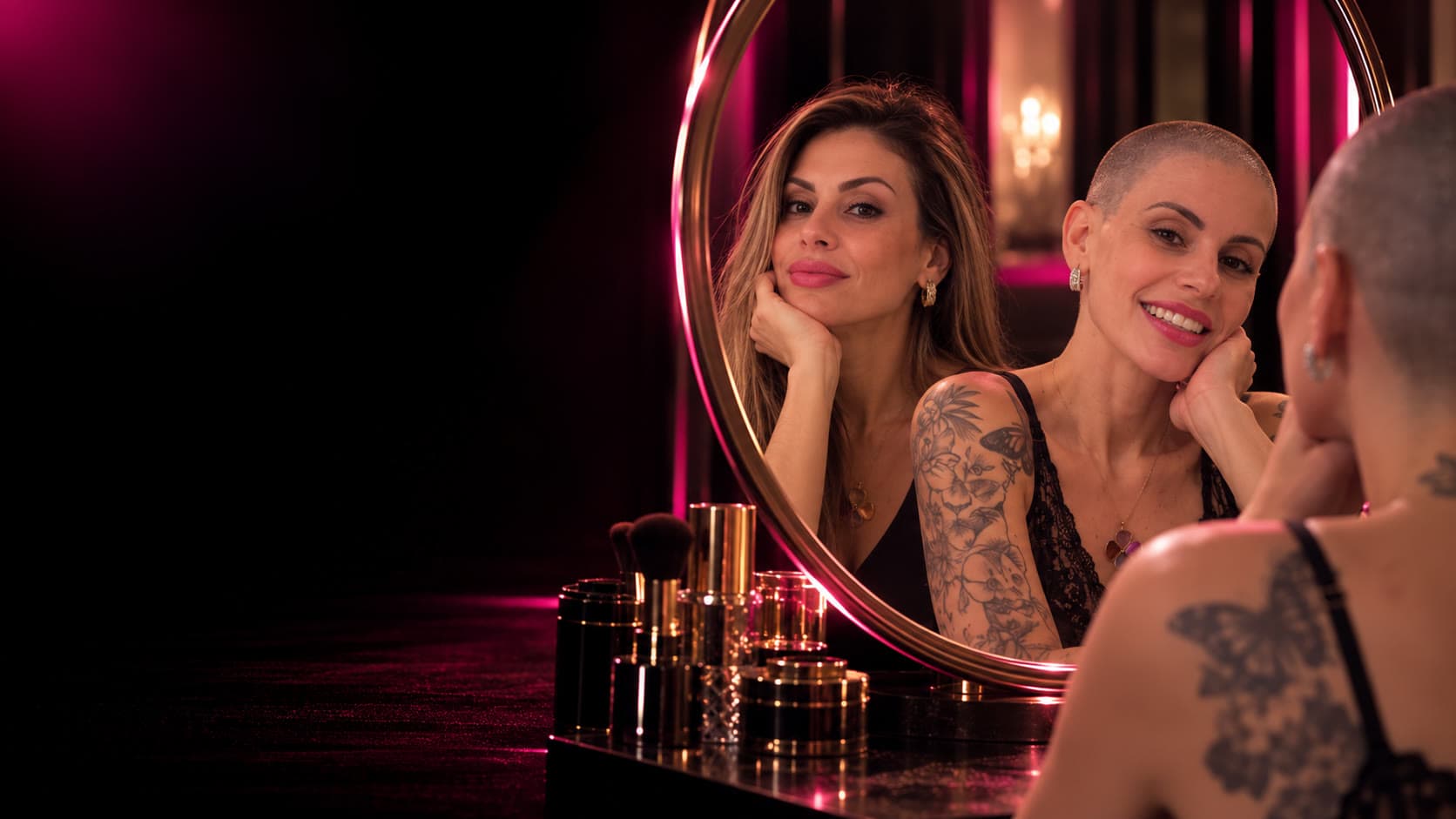 Ana Liz diante do espelho, com uma amiga refletida ao lado