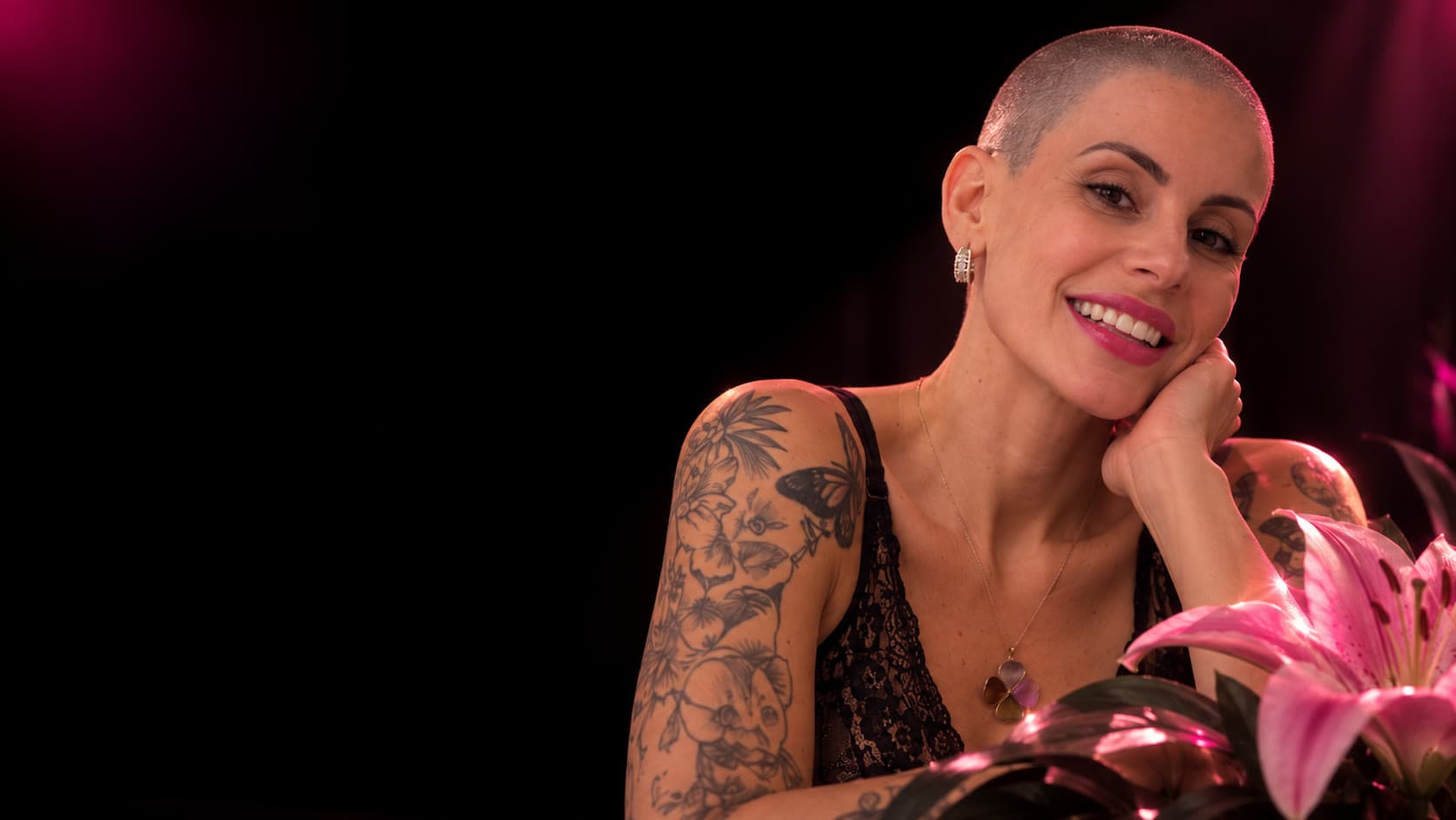 Ana Liz sorrindo, com tatuagens no braço e um lírio rosa
